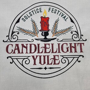 May include: An embroidered design in black and white featuring a candle with green pine branches, a black candle holder, and the text "Solstice Festival Candlelight Yule".