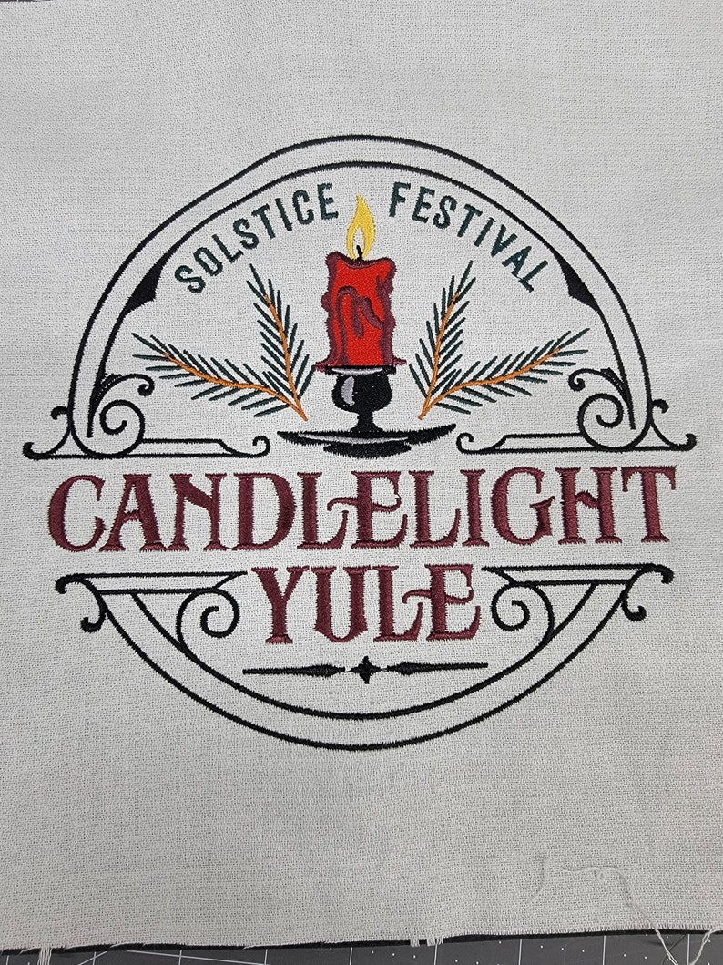 May include: An embroidered design in black and white featuring a candle with green pine branches, a black candle holder, and the text "Solstice Festival Candlelight Yule".