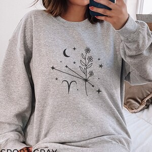 May include: A gray sweatshirt with a black floral design and the zodiac symbol Aries. The text "SPORT GRAY" is printed on the bottom of the sweatshirt.