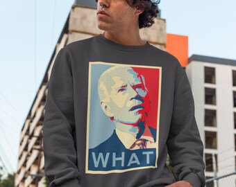 May include: A dark grey sweatshirt featuring a graphic of a man's face in a red, white and blue colour scheme. The text "WHAT" is printed below the image.