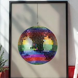 May include: A framed print of a multi-coloured disco ball, suspended against a neutral backdrop. The ball is made up of many small, reflective squares, creating a shimmering effect. The artwork is framed in black, adding a touch of contrast to the vibrant colours.