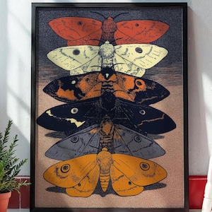 Puede incluir: Una impresión artística enmarcada que presenta cinco polillas estilizadas dispuestas verticalmente. Las polillas son en tonos de naranja, crema, negro, gris y amarillo. El fondo tiene un degradado de azul oscuro a marrón claro.