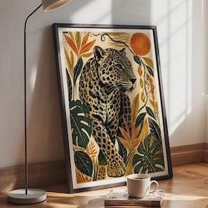 Könnte beinhalten: Ein gerahmter Kunstdruck mit einem Leoparden, umgeben von tropischem Blattwerk, darunter Monstera-Blätter und orangefarbene Blüten, vor einem cremefarbenen Hintergrund mit einer kreisförmigen orangefarbenen Sonne, in einem schwarzen Rahmen.