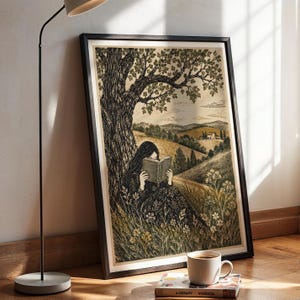 Puede incluir: Una lámina artística enmarcada que presenta una ilustración en blanco y negro de una persona sentada bajo un gran árbol leyendo un libro en un campo de hierba con colinas al fondo. La lámina está colocada en un marco negro sobre el suelo.
