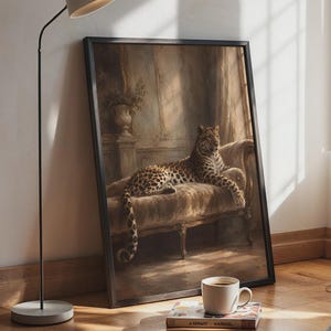 May include: A framed wall art print featuring a leopard resting on a velvet chaise lounge in a dimly lit room with a stone pedestal and plant. The artwork is displayed in a thin black frame, leaning against a wall next to a floor lamp.