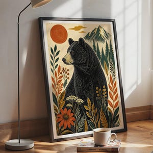 Könnte beinhalten: Ein gerahmter Kunstdruck mit einem schwarzen Bären inmitten von orangefarbenen Blumen, grünem Blattwerk und weißen Wildblumen. Der Hintergrund zeigt eine große orangefarbene Sonne, ein Gebirge und einen Kiefernwald in einem illustrierten Stil.