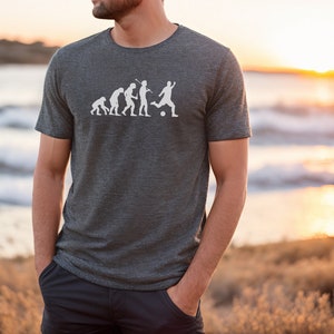 May include: A dark grey t-shirt with a white graphic of the evolution of man, ending with a man kicking a football.