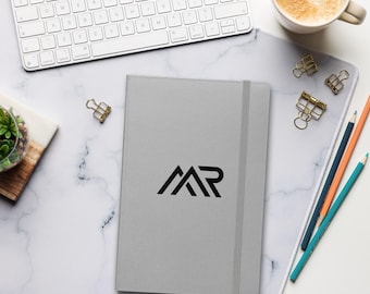 May include: A gray notebook with a black elastic closure and the letters "AR" in black on the front.