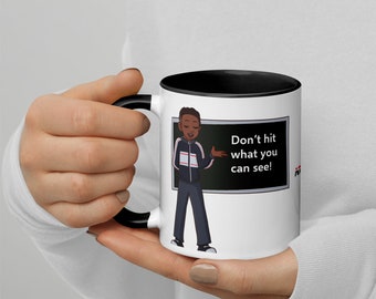 May include: White ceramic mug with a black rim and handle. The mug features a cartoon illustration of a person standing in front of a chalkboard with the text "Don't hit what you can see!"