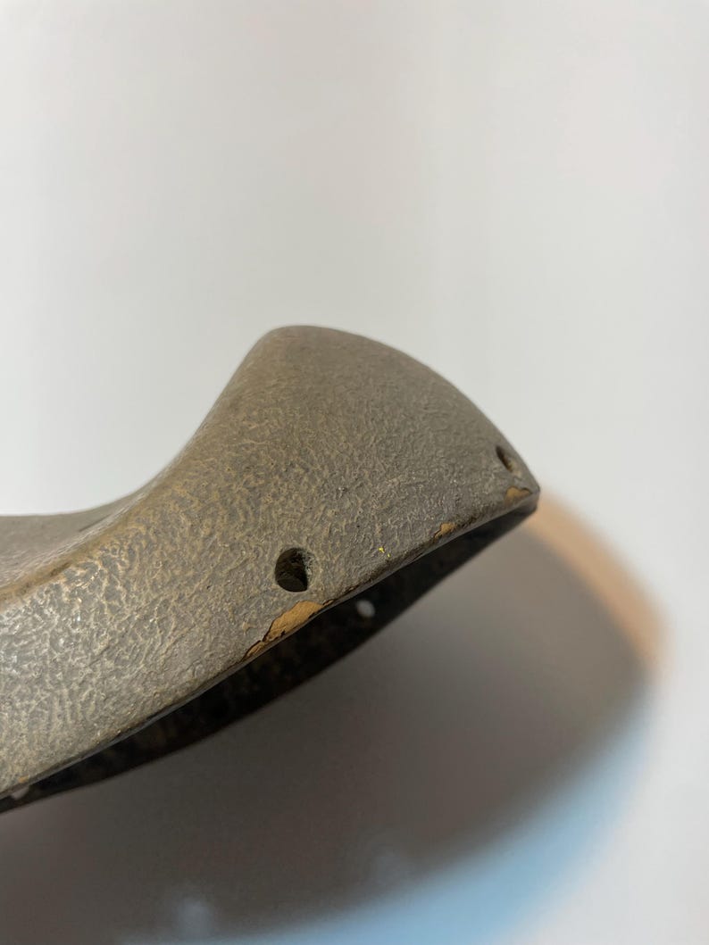 May include: Close-up of a weathered, grey object with a textured surface. The object has a curved shape with two small holes near the edge. The edges show signs of wear and tear, with some areas of discolouration.