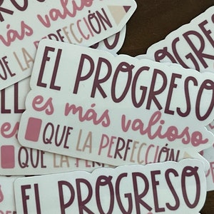 May include: A set of pink and brown stickers with the Spanish phrase "El progreso es más valioso que la perfección" which translates to "Progress is more valuable than perfection".