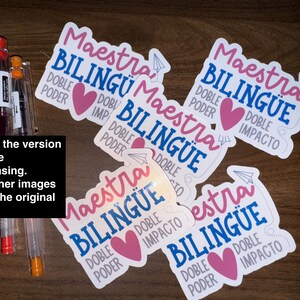 May include: White stickers with the text "Maestra Bilingüe" in pink and blue, featuring a pink heart and paper airplane design. The stickers also include the words "Doble Poder" and "Doble Impacto".