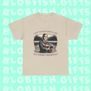 May include: A beige t-shirt with a graphic of a man holding a fish in a lake, with trees in the background. The text reads "I KNOW THE HUMAN BEING AND FISH CAN COEXIST PEACEFULLY". This is a casual wear item.