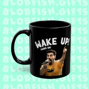 Könnte beinhalten: Schwarze Keramik-Kaffeetasse mit einer weißen Grafik eines Mannes, der ein Mikrofon hält, und dem Text "WAKE UP! (WAKE UP)"