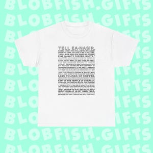 Puede incluir: Camiseta blanca con el texto "TELL EA-NASIR" y un largo mensaje impreso en gris. El texto parece ser un texto histórico o antiguo, posiblemente una queja o una carta. La camiseta es una prenda informal.