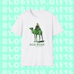 May include: White t-shirt with a green camel and a person riding it. The text "SILK ROAD" is printed below the image, with the words "Anonymous Market" in smaller font below that.