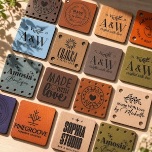 May include: A selection of square leather tags in various colours, each with unique text and designs. The tags feature phrases like "Made with Love," brand names, and logos. Some tags have decorative stitching around the edges.