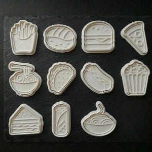 May include: A white ceramic mug with a black handle and the text "But First, Coffee" in a bold, black font. The mug is set against a blurred background, suggesting a cozy setting.