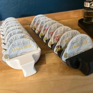 May include: Two white and black plastic dispensers with individual cocktail pods. The white dispenser has a label that reads "BARTESIAN LEMON DROP LEAD VODKA". The black dispenser has a label that reads "BARTESIAN LEMON DROP LEAD VODKA".