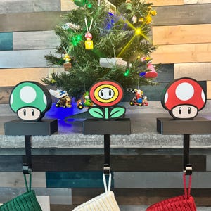 May include: Three black stocking holders with a green, red, and yellow mushroom-shaped topper. The holders are decorated with a black base and a metal hook.