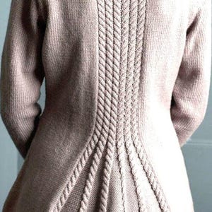 May include: A light brown knitted sweater with a detailed cable knit design down the back. The sweater has long sleeves and a flared peplum-style hem. The cable knit detail adds texture and visual interest to the garment.