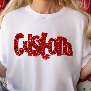 May include: White t-shirt with the word "Custom" in red glitter letters.