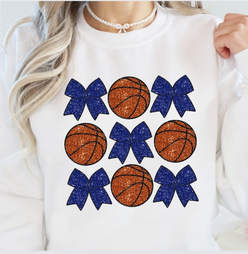 May include: White sweatshirt with a design of orange basketballs and blue glitter bows.