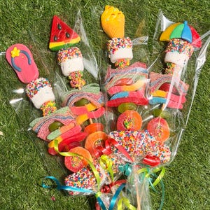May include: Three candy skewers wrapped in clear plastic, each featuring a variety of colorful gummy candies, marshmallows covered in rainbow sprinkles, and a themed topper shaped like a flip-flop, a watermelon slice, or a beach umbrella.