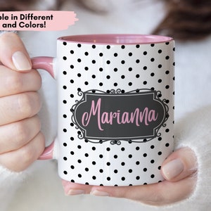 May include: White ceramic mug with a pink rim and black polka dots. The mug has a black frame with the name "Marianna" written in pink inside.