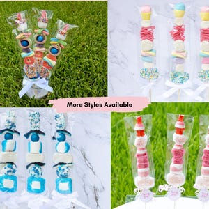 Pu&ograve; includere: Spiedini di marshmallow in confezioni trasparenti di cellophane. Gli spiedini presentano marshmallow, caramelle e zuccherini colorati. Alcuni spiedini hanno un tema a coniglietto. L'immagine include il testo "More Styles Available".