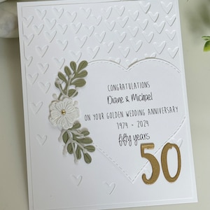 May include: A white card with a heart-shaped design featuring green leaves and white flowers. The card reads "Congratulations Diane & Michael on your Golden Wedding Anniversary 1974 - 2024 fifty years 50".