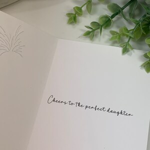 May include: A white card with the text "Cheers to the perfect daughter" written in black cursive.