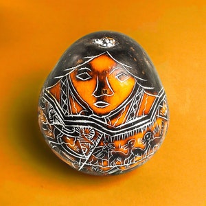 Può includere: Una zucca con un disegno intagliato di un viso di donna e un motivo geometrico. La zucca è dipinta in bianco e nero su uno sfondo giallo.