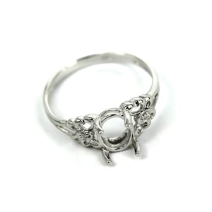 May include: Silver ring setting with a filigree design and a round bezel for a gemstone. The ring has a delicate floral pattern with small accents.