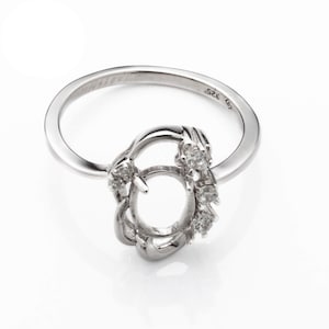 May include: A silver ring with a round setting and small diamonds around the setting. The ring is marked "925".