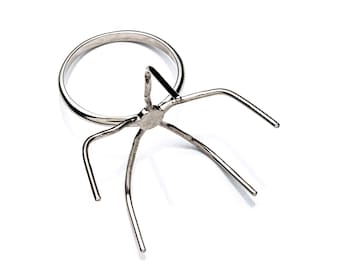 May include: A silver ring stand with a circular base and five prongs extending from the center. The stand is designed to hold a ring securely.