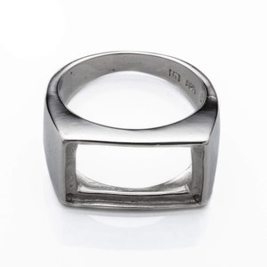 May include: A silver ring with a square-shaped cutout in the center. The ring is made of metal and has a polished finish.