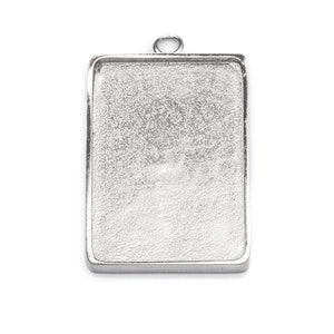 May include: Silver-toned metal pendant tray with a rectangular shape and a loop at the top for hanging.