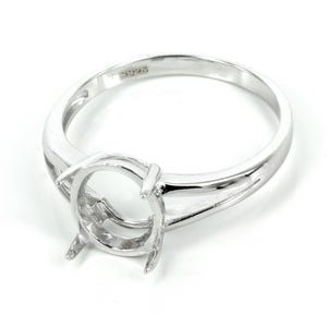 May include: Sterling silver ring setting with a round bezel for a gemstone. The ring has a delicate, openwork design on the band.