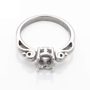 May include: A silver ring with a delicate, ornate design. The ring has a center setting for a stone, with two smaller decorative elements on either side.