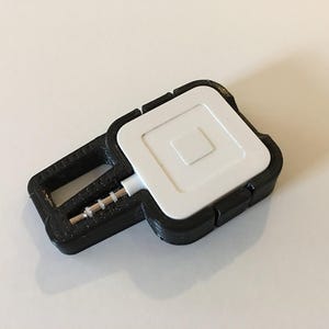 May include: A black and white Square card reader with a 3.5mm audio jack. The reader is encased in a black, key-shaped holder. The white card reader has a square design with a smaller square in the centre.