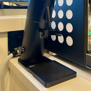 May include: A black coffee grinder with a silver knob and a black drip tray. The grinder is sitting on a white countertop.