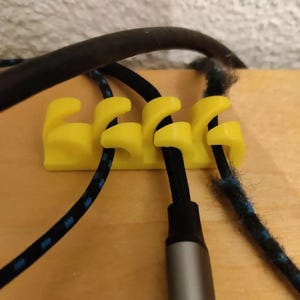 May include: A yellow cable organizer with four slots, holding black and blue cables. The organizer is made of plastic and is designed to keep cables tidy. The cables are of varying thicknesses and have silver and black connectors.
