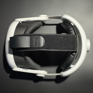May include: White and black VR headset with adjustable head strap and cushioned ear pads. The headset features the text "KIWI design" on the strap. The device is designed for virtual reality gaming and entertainment.