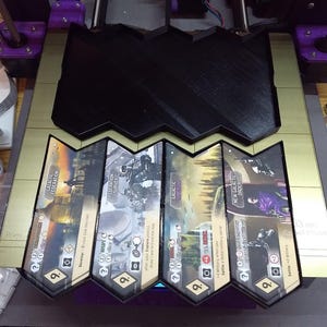 May include: A black, 3D-printed game board with a distinctive, angular design. Four game cards are visible, each with a different title: "Galactic Federation", "Federation Survey", "Galactic Imperium", and "New Galactic Order". The cards feature illustrations and game instructions.
