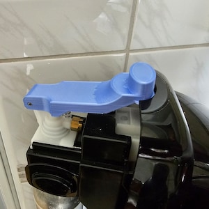 以下が含まれることがあります： 黒と白の機器に取り付けられた青い3Dプリントレバーのクローズアップ。レバーは片手で操作できるように設計されています。