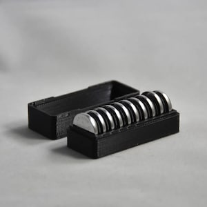 May include: A white ceramic mug with a black handle and the text "But First, Coffee" in a bold, black font. The mug is set against a blurred background, suggesting a cozy setting.