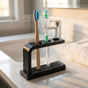 May include: A black toothbrush holder with two toothbrushes. One toothbrush has a wooden handle and blue bristles, the other has a clear handle and green bristles. The holder is on a white countertop.