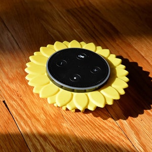 Peut inclure: Un support en silicone jaune en forme de tournesol pour un haut-parleur intelligent Amazon Echo Dot noir. Le haut-parleur a quatre boutons : volume haut, volume bas, action et désactivation du microphone.
