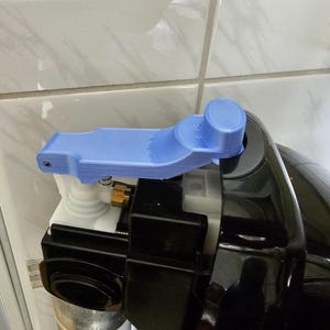 Pode incluir: Uma alavanca azul clara, impressa em 3D, presa a um aparelho preto e branco. A alavanca tem uma extremidade cilíndrica e um design curvo e estriado. O aparelho tem um encaixe metálico e um cilindro prateado.